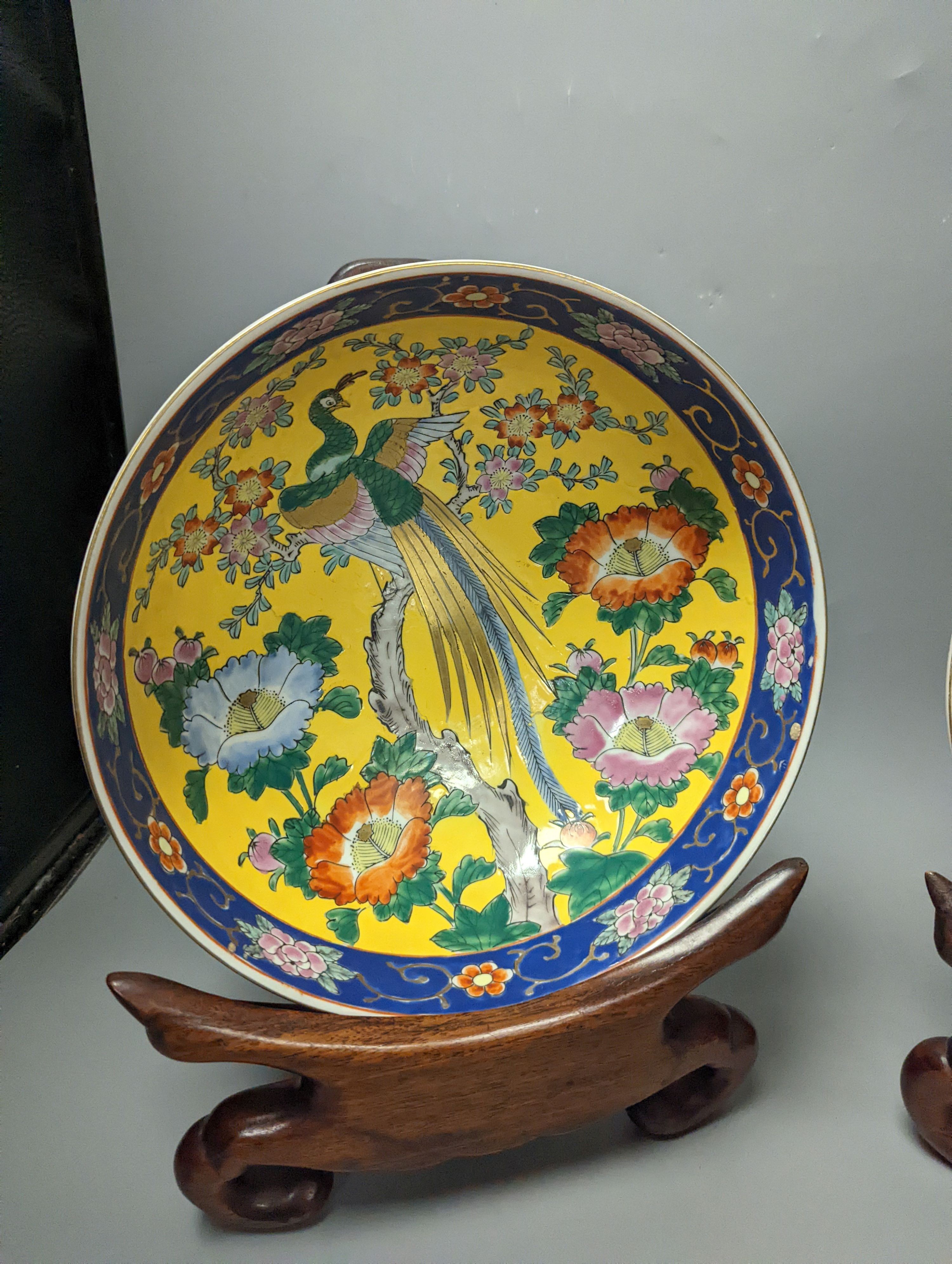 A Japanese Satsuma vase of a geisha and two Japanese yellow and a blue ground bowls each on wooden stands, Stands 32 cms high x 26cms deep.